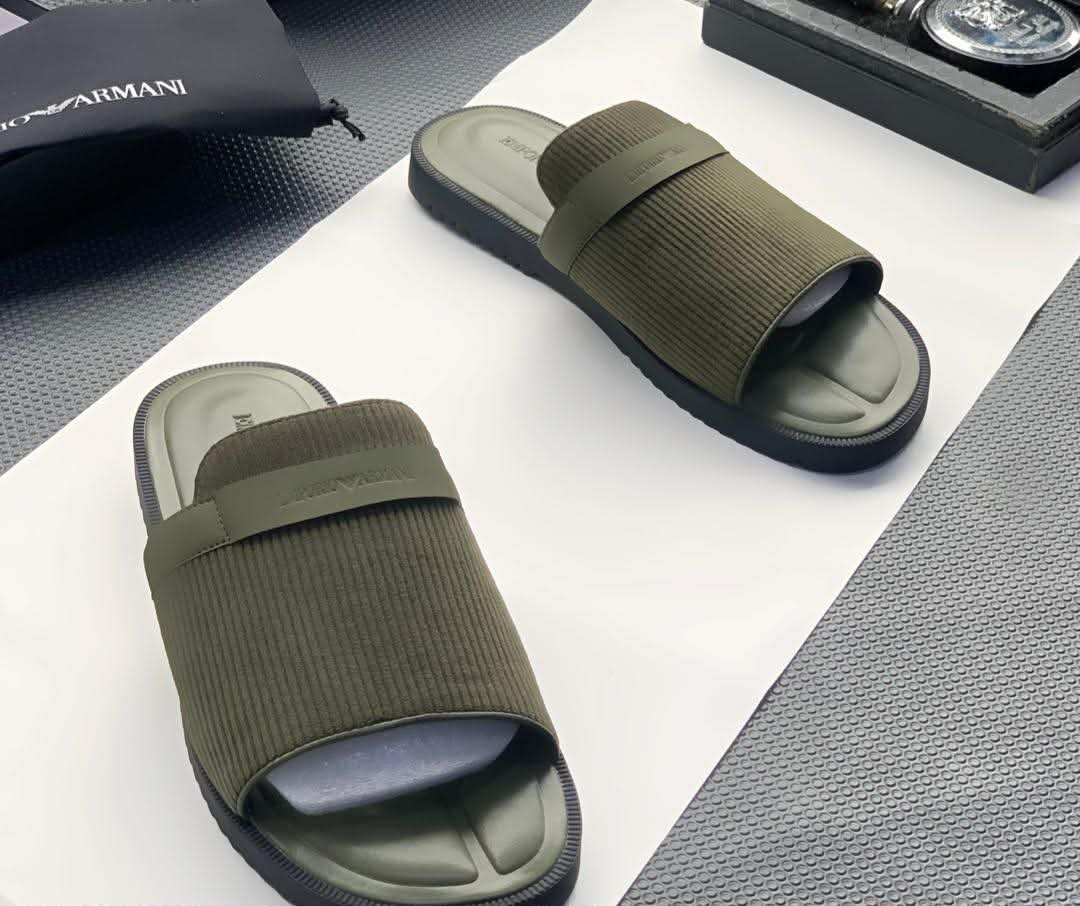 root A pair of green ribbed slide sandals from Armani, displayed on a white surface with a black pouch and watch in the background, embodying Modern Luxury and Urban Edge.
