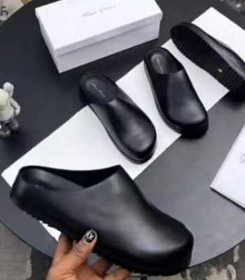 A pair of black leather clog shoes with a comfortable thick sole, presented on a stylish black table with a white box and cloth, exuding luxury and sophistication.