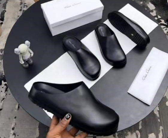 root A pair of black leather clog shoes with a comfortable thick sole, presented on a stylish black table with a white box and cloth, exuding luxury and sophistication.