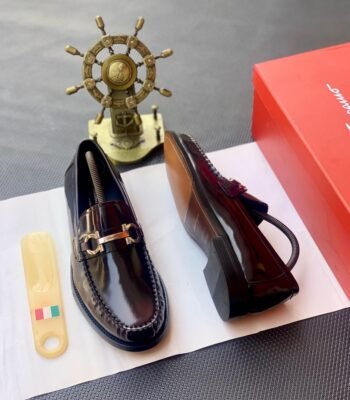 A pair of luxurious burgundy loafers with gold buckle details, presented on a white paper with a shoe horn and red shoe box, exuding Modern Luxury and Urban Edge style.