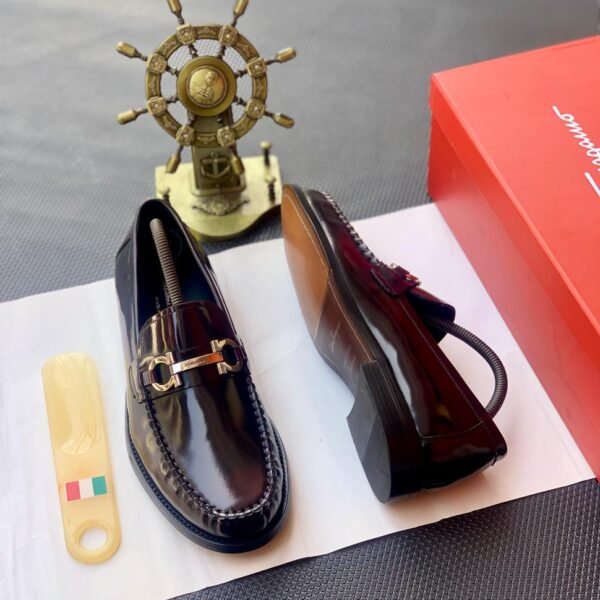 A pair of luxurious burgundy loafers with gold buckle details, presented on a white paper with a shoe horn and red shoe box, exuding Modern Luxury and Urban Edge style.