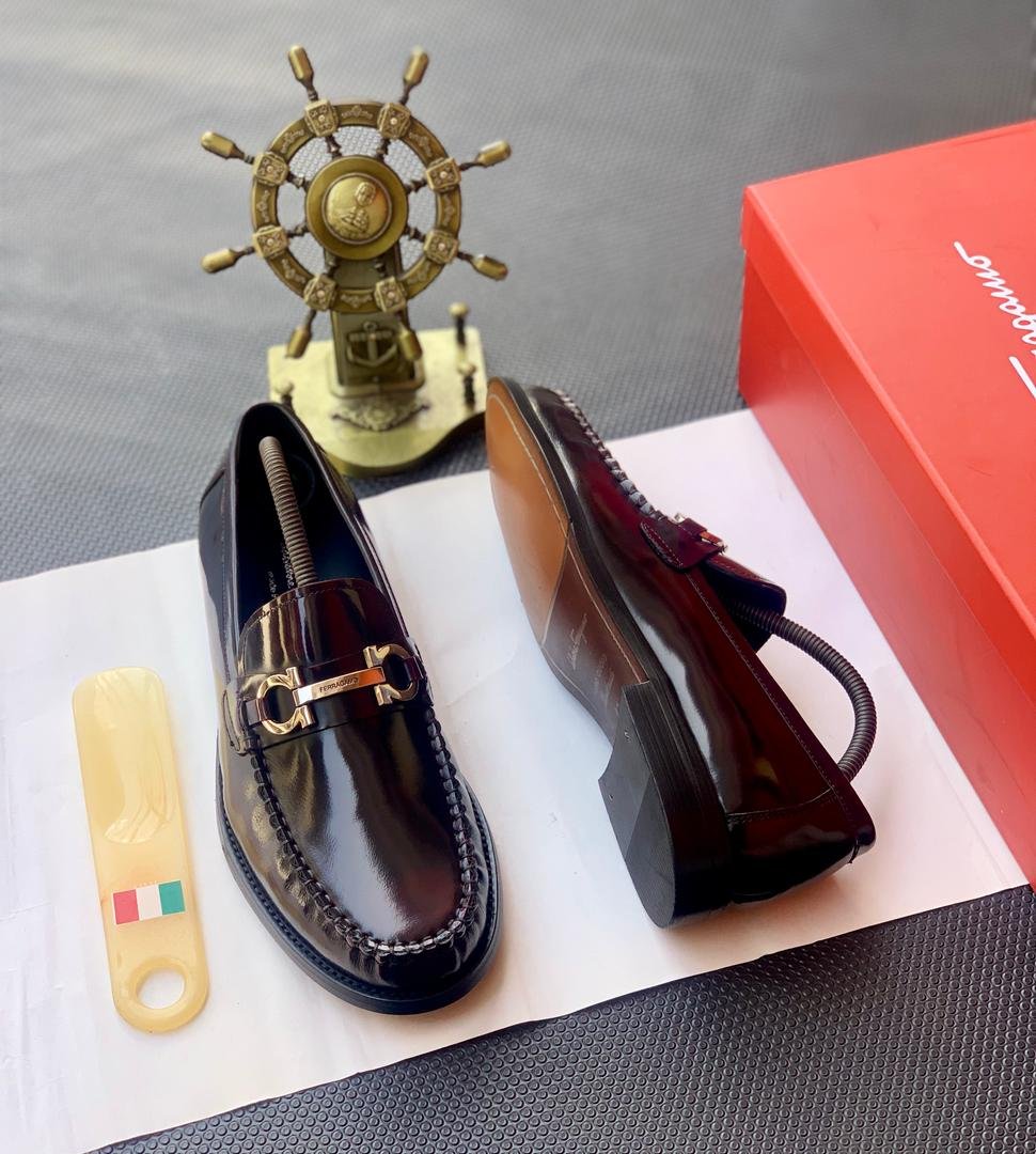 root A pair of luxurious burgundy loafers with gold buckle details, presented on a white paper with a shoe horn and red shoe box, exuding Modern Luxury and Urban Edge style.
