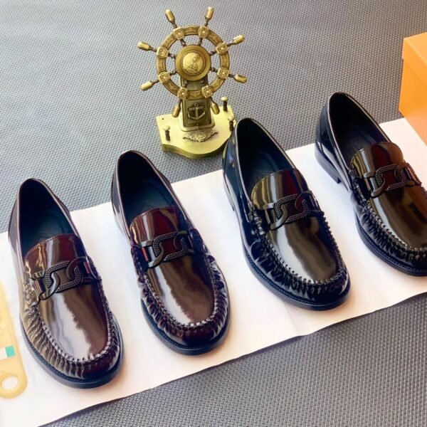 Four pairs of black leather loafers with sleek buckle detailing, showcasing modern luxury and urban edge, on a white paper with a golden ship's wheel in the background.