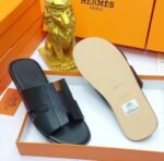 Black leather slide sandals in an orange box with a gold lion figurine, embodying modern luxury and timeless quality.