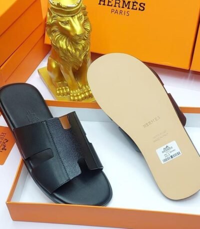 Black leather slide sandals in an orange box with a gold lion figurine, embodying modern luxury and timeless quality.