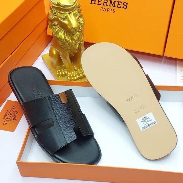 Black leather slide sandals in an orange box with a gold lion figurine, embodying modern luxury and timeless quality.