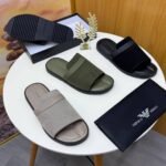 A pair of green ribbed slide sandals from Armani, displayed on a white surface with a black pouch and watch in the background, embodying Modern Luxury and Urban Edge.