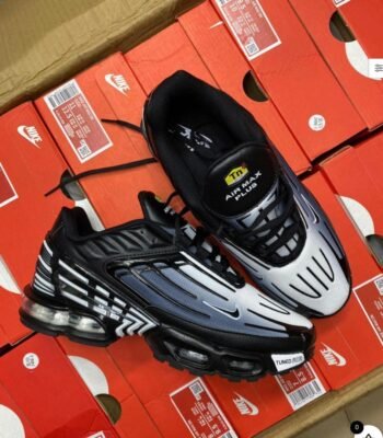 A pair of black and white Nike Air Max Plus sneakers on top of red shoe boxes, embodying Modern Luxury and Urban Edge.