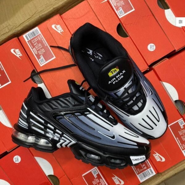 A pair of black and white Nike Air Max Plus sneakers on top of red shoe boxes, embodying Modern Luxury and Urban Edge.