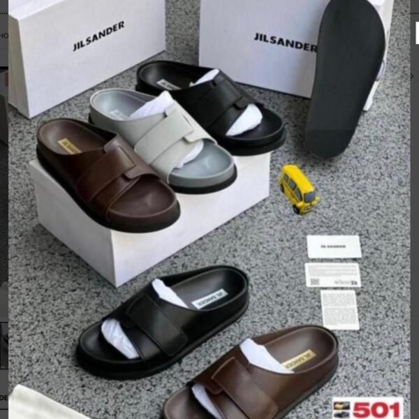 A display of Jil Sander two-strap leather slides in brown and black, accompanied by their signature boxes and packaging, embodying Modern Luxury and Urban Edge.
