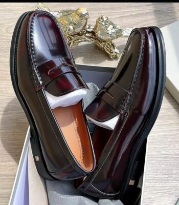 A pair of luxurious burgundy leather loafers in a shoe box, showcasing modern luxury and urban edge with impeccable craftsmanship.