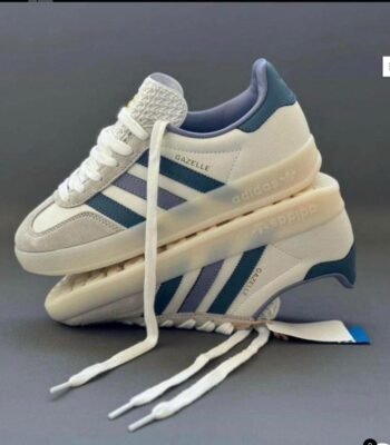 A pair of white and blue Adidas Gazelle Indoor sneakers stacked on top of each other, showcasing the shoe's sleek design and Urban Edge style.