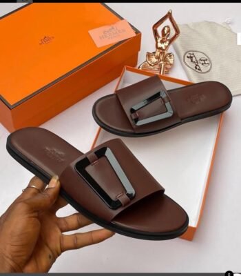 Brown leather slide sandals with metal buckle, presented with orange box and accessories, showcasing Modern Luxury and Urban Edge.