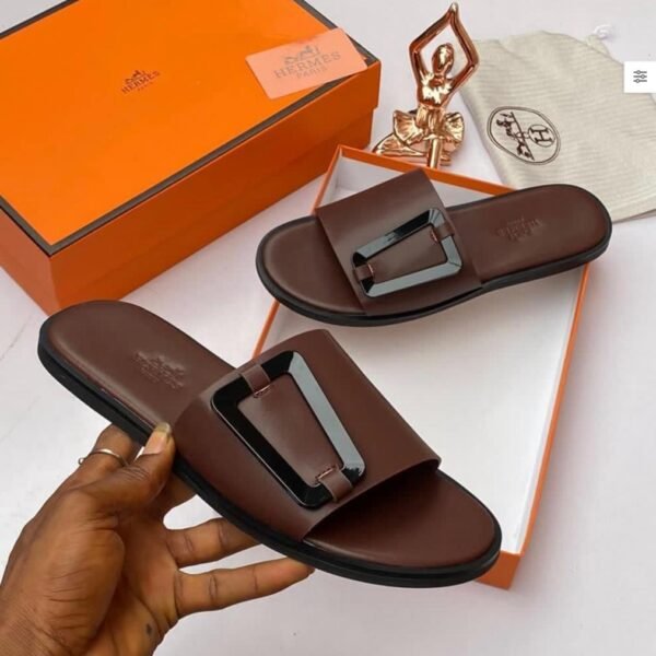 Brown leather slide sandals with metal buckle, presented with orange box and accessories, showcasing Modern Luxury and Urban Edge.