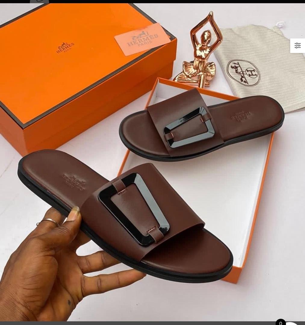 IMG-20260610-WA0023 Brown leather slide sandals with metal buckle, presented with orange box and accessories, showcasing Modern Luxury and Urban Edge.