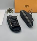 A pair of black leather UGG sandals with metal buckles and laces, exuding modern luxury and urban edge.