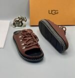 A pair of black leather UGG sandals with metal buckles and laces, exuding modern luxury and urban edge.