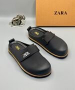 A pair of black leather clogs with gold accents and ZARA logo, showcasing modern luxury and urban edge.