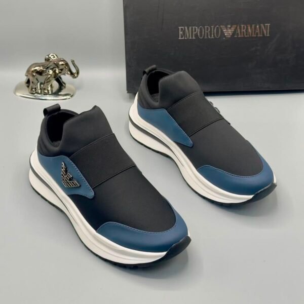 A pair of black and blue Emporio Armani sneakers with white soles, showcased with a silver elephant statue and a black Emporio Armani box in the background.