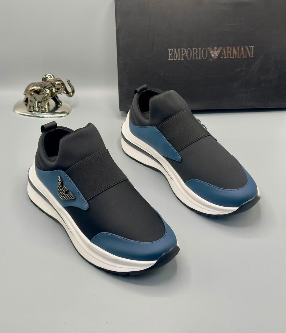 root A pair of black and blue Emporio Armani sneakers with white soles, showcased with a silver elephant statue and a black Emporio Armani box in the background.