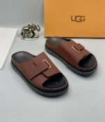Grey UGG slide sandals with zigzag stitching and gold-tone buckle on a white surface, exuding Modern Luxury and Urban Edge.