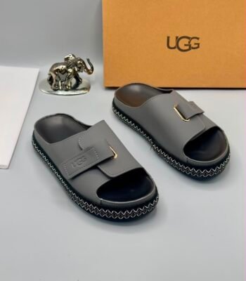 Grey UGG slide sandals with zigzag stitching and gold-tone buckle on a white surface, exuding Modern Luxury and Urban Edge.