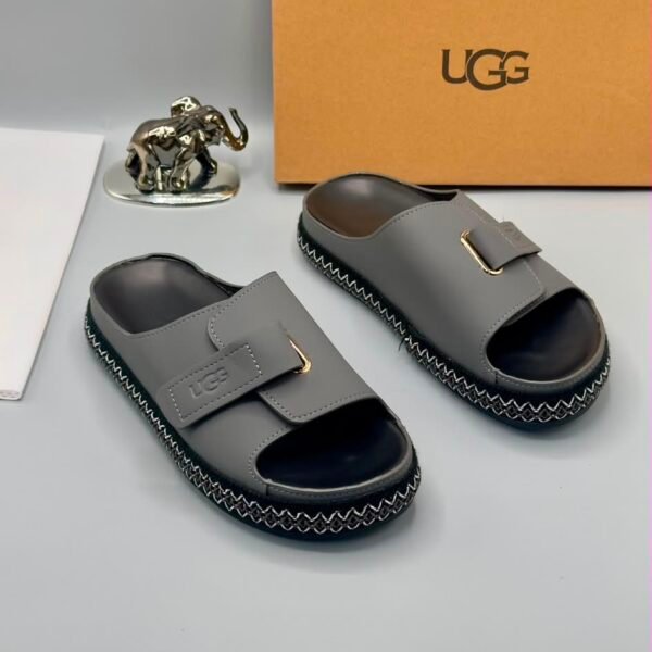 Grey UGG slide sandals with zigzag stitching and gold-tone buckle on a white surface, exuding Modern Luxury and Urban Edge.