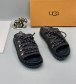 A pair of black leather UGG sandals with metal buckles and laces, exuding modern luxury and urban edge.