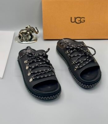 A pair of black leather UGG sandals with metal buckles and laces, exuding modern luxury and urban edge.