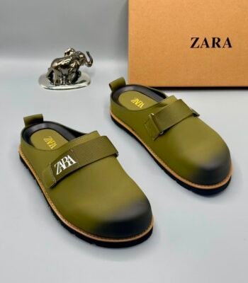 A pair of olive green strap shoes with a silver elephant statue and Zara box in the background, showcasing Modern Luxury and Urban Edge style.