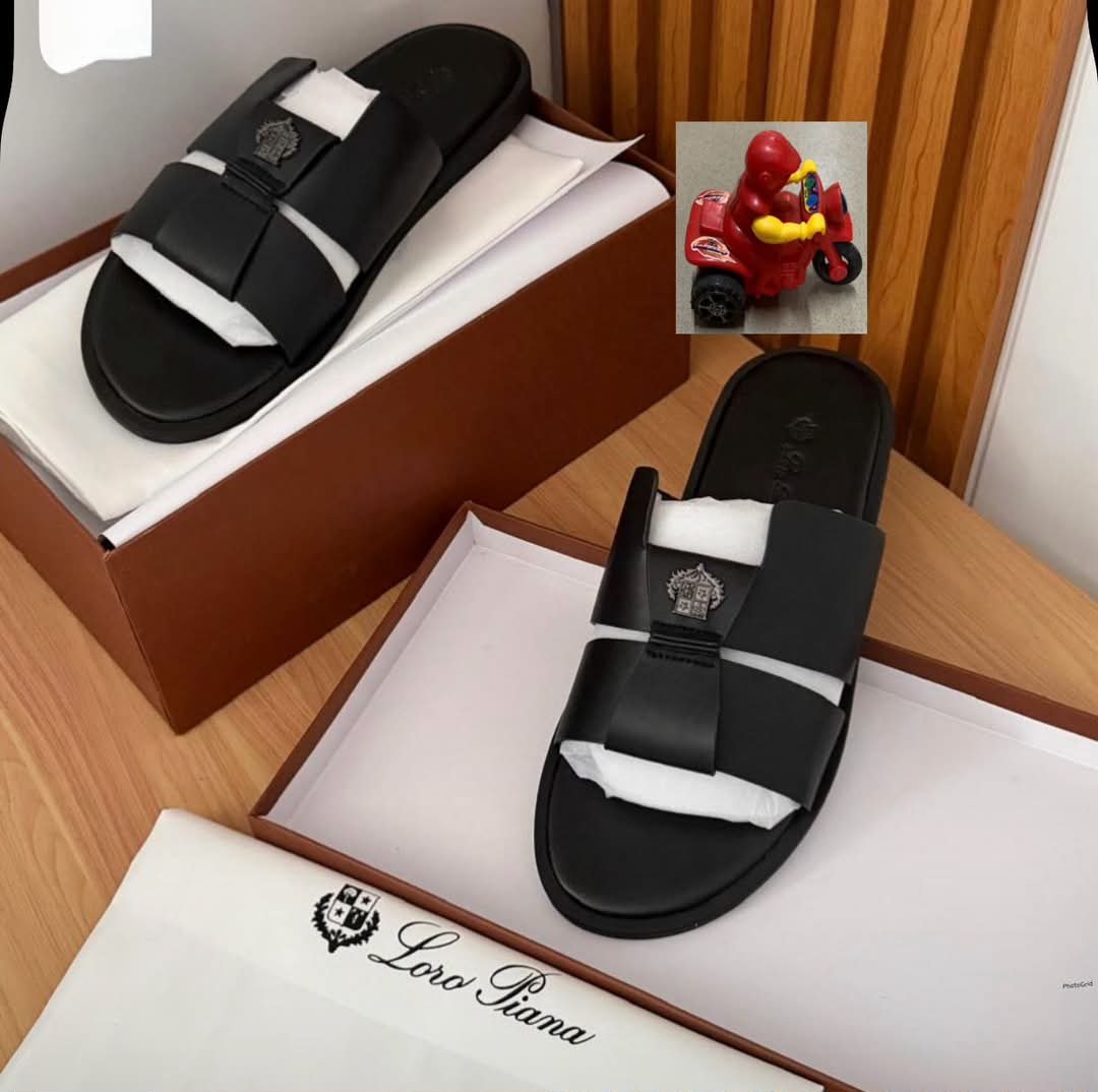 root A pair of black leather slides with two straps and an emblem logo, placed on white paper inserts in brown shoe boxes, showcasing Modern Luxury and Urban Edge.