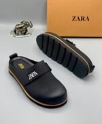 A pair of black leather clogs with gold accents and ZARA logo, showcasing modern luxury and urban edge.