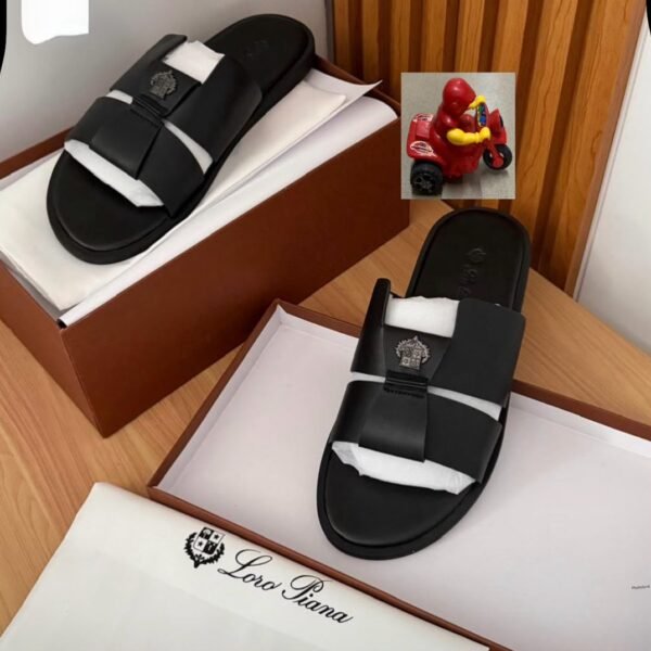 Luxurious black slides with two straps and a logo on top, placed in a brown shoe box with white tissue paper, embodying Modern Luxury and Urban Edge in Nigeria.