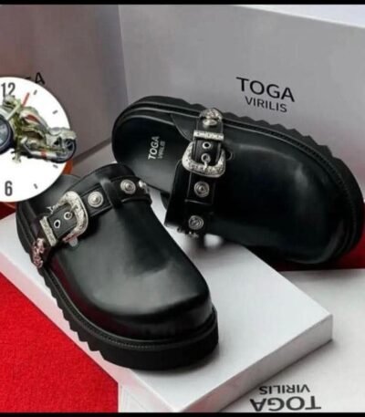 A pair of sleek black leather shoes with silver buckles, presented on a white box with the brand name 'TOGA VIRILIS' and a red carpet background, embodying Modern Luxury and Urban Edge in Nigeria.