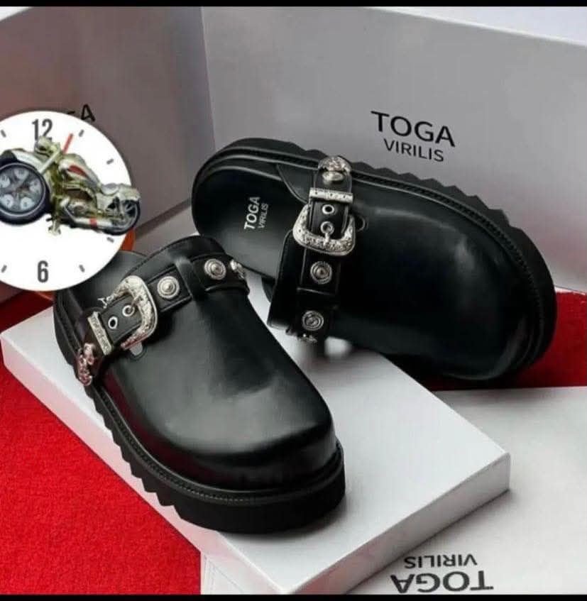 root A pair of sleek black leather shoes with silver buckles, presented on a white box with the brand name 'TOGA VIRILIS' and a red carpet background, embodying Modern Luxury and Urban Edge in Nigeria.