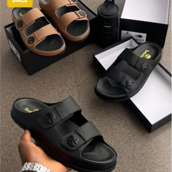 Modern luxury sandals in sleek black and tan colors, displayed with their boxes and a water bottle, embodying urban edge and timeless quality.