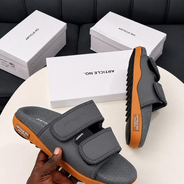 Modern luxury grey and orange sandals with white shoe boxes on a table, embodying urban edge and timeless quality.