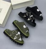Luxury chunky sandals in black and green, featuring two wide straps with silver buckles, displayed on a wooden surface with Alexander McQueen packaging.