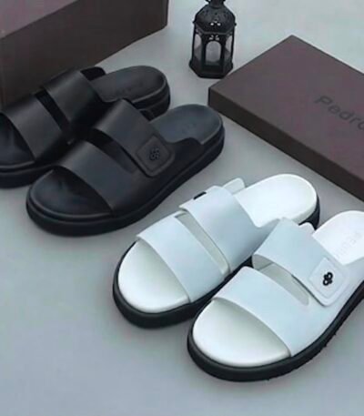 Two pairs of stylish slides, one in sleek black and the other in pristine white, displayed with brown shoe boxes and a lantern, embodying modern luxury and urban edge.