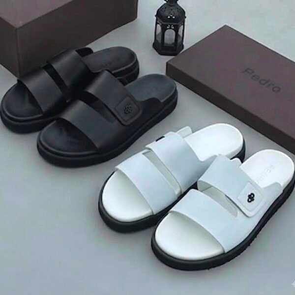 Two pairs of stylish slides, one in sleek black and the other in pristine white, displayed with brown shoe boxes and a lantern, embodying modern luxury and urban edge.