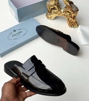 A sleek black Prada half shoes with a glossy finish, presented with its box and packaging, exuding modern luxury and urban edge.