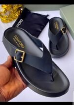 A pair of luxurious black slides with gold buckles, presented on a white surface with a black pouch and box in the background.