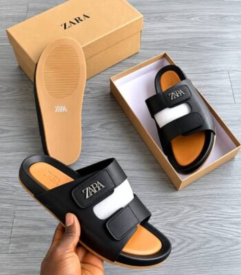 A pair of black and white slides with the ZAPA logo, displayed in a box and held by a hand, showcasing Modern Luxury and Urban Edge style.