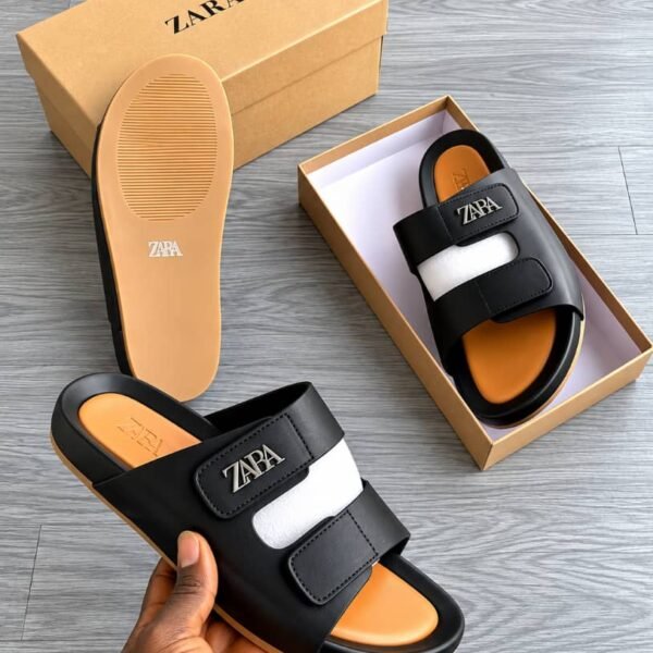 A pair of black and white slides with the ZAPA logo, displayed in a box and held by a hand, showcasing Modern Luxury and Urban Edge style.