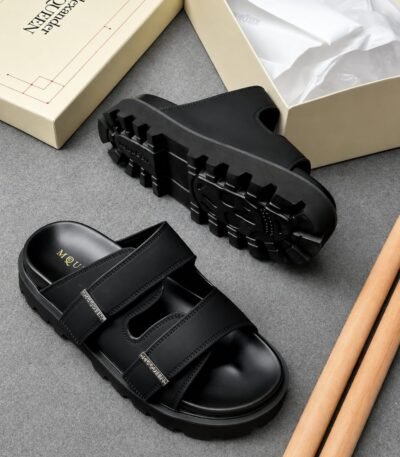 A pair of black leather sandals with a rugged sole and double strap design, presented with a shoe box and tissue paper, exuding Modern Luxury and Urban Edge.