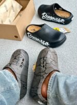 A pair of black clogs with white Bonanza Storm Rider branding and a pair of grey clogs with a cracked pattern, showcasing modern luxury footwear.