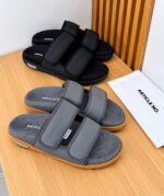 A pair of black slides with orange soles, presented on a white table with white boxes in the background, embodying Modern Luxury and Urban Edge.