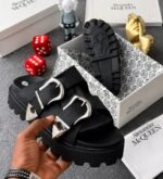 A pair of black sandals with silver buckles, showcased in a luxurious setting with Alexander McQueen branding, exuding Modern Luxury and Urban Edge.