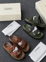 A pair of black sandals with silver buckles, showcased in a luxurious setting with Alexander McQueen branding, exuding Modern Luxury and Urban Edge.