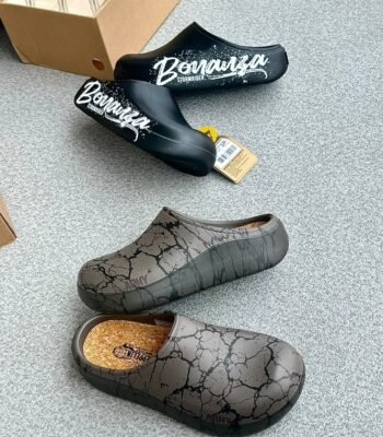 A pair of black clogs with white Bonanza Storm Rider branding and a pair of grey clogs with a cracked pattern, showcasing modern luxury footwear.